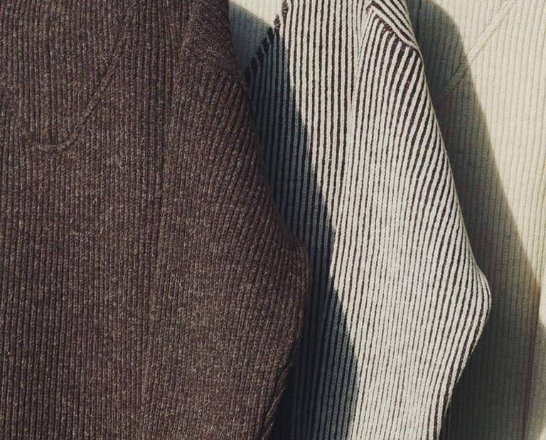 drei Troyer der Marke piies hängen auf einem Kleiderbügel in der Natur, ein dunkler, ein gestreifter