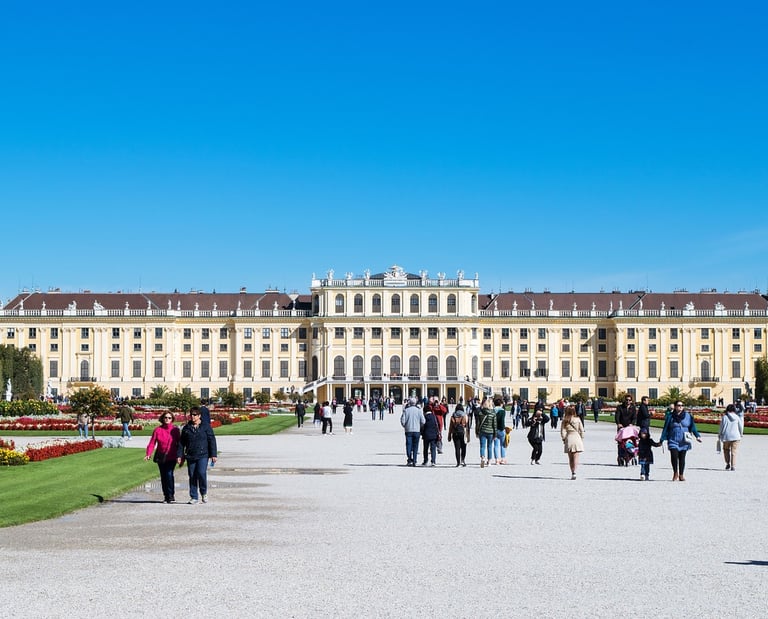 Fachada principal del Palacio de Schönbrunn en Viena con turistas paseando por los jardines