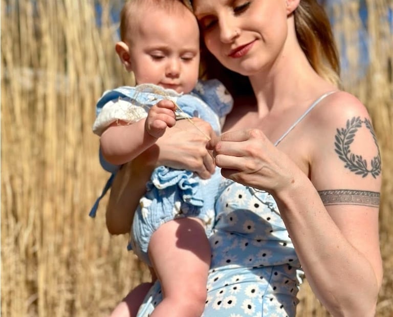A mother and baby girl both wearing matching blue dresses in a hay field on a sunny day, symboling maternal love.