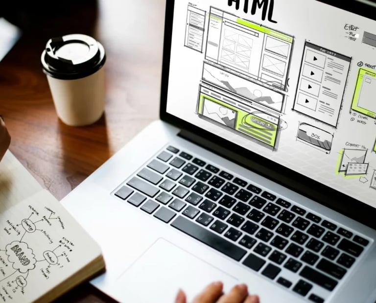 Wireframe de sitio web en una laptop y una persona escribiendo ideas en un cuaderno