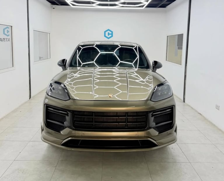 A gold Porsche Cayenne luxury SUV parked in a brightly lit garage with honeycomb LED ceiling lights.
