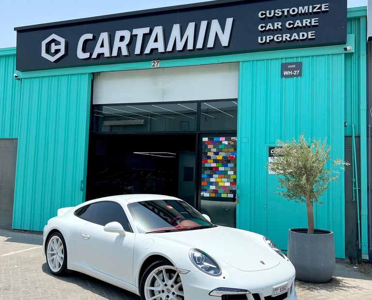 White Porsche sports car parked outside Cartamin car care and customization shop.