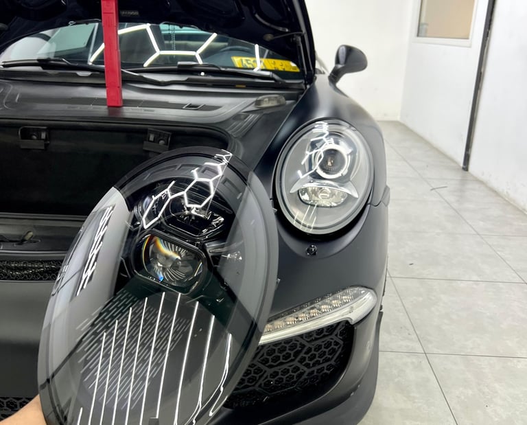 Close-up of a custom black LED headlight being installed on a matte black Porsche 911 GT3.