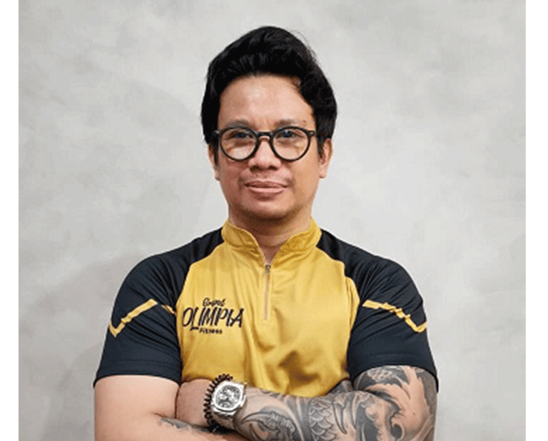 Professional fitness trainer with arm tattoos wearing a yellow and black Olimpia gym shirt.