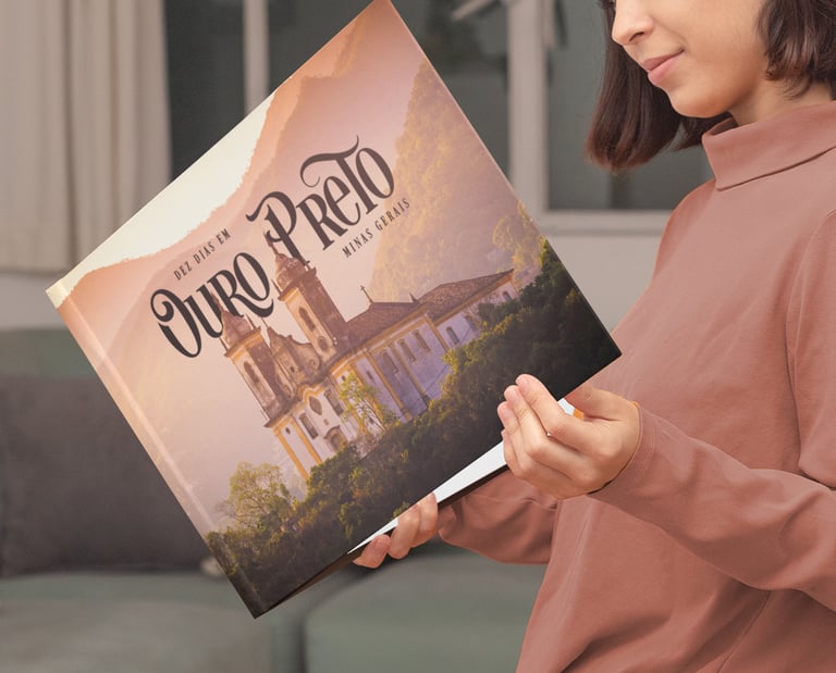 Mulher sorrindo ao folhear álbum de viagem personalizado de Ouro Preto na sala de estar.