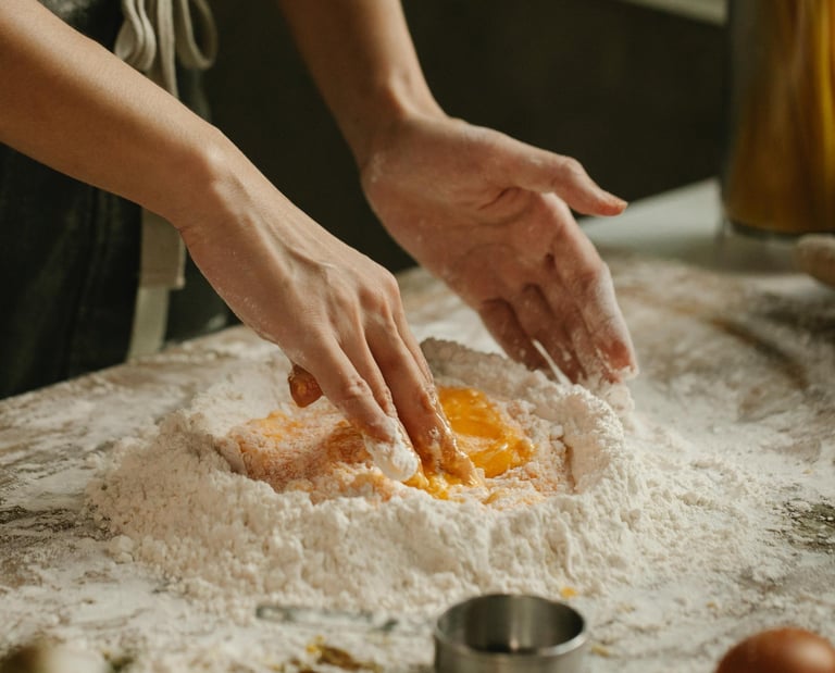 A chef's hands mixing fresh egg yolks into a mound of flour to make homemade pasta dough.