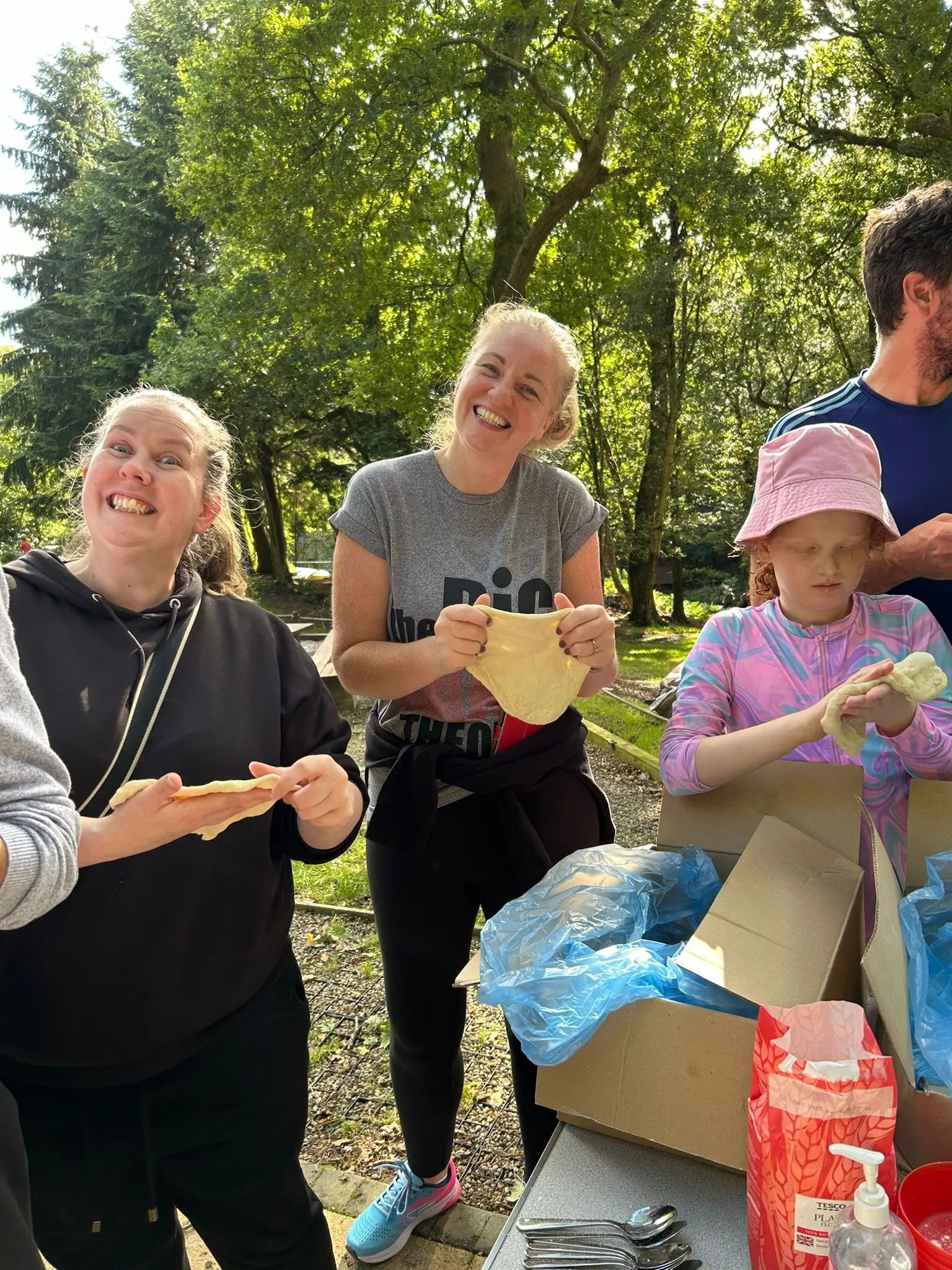 Two leaders smile at the camera while stretching dough for the 25th Allerton scout camp