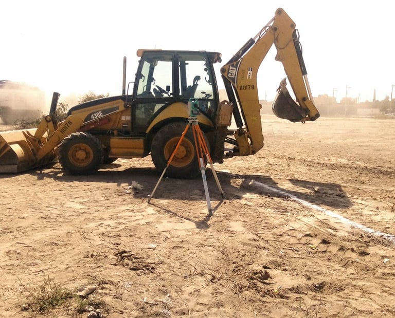 Yellow Cat backhoe loader and surveying equipment on a dusty construction site for land excavation.
