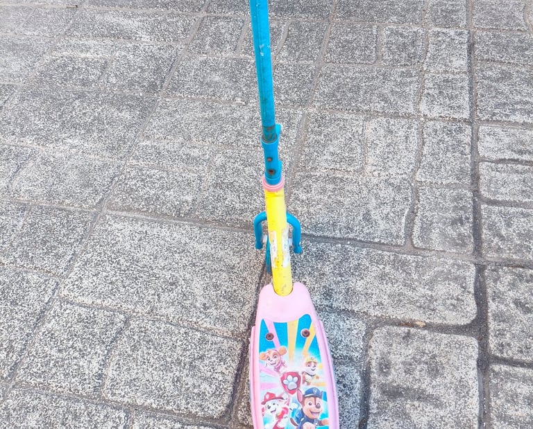 Vista frontal da trotinete Paw Patrol Smobe azul e amarela com plataforma rosa, apoiada na calçada