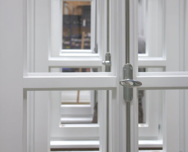 etailaufnahme weiß lackierter Holzfenster mit silbernem Griff und Blick durch mehrere Fensterebenen.