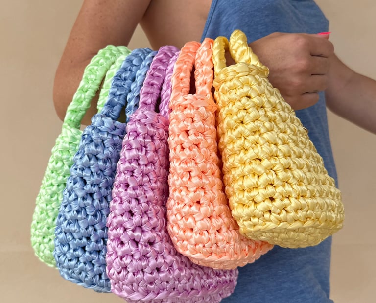 Handmade pastel crochet mini bags in lime, blue, pink, orange, and yellow held by a woman.