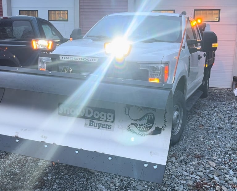 a white truck with a silver plow blade on the front with its lights above the plow on