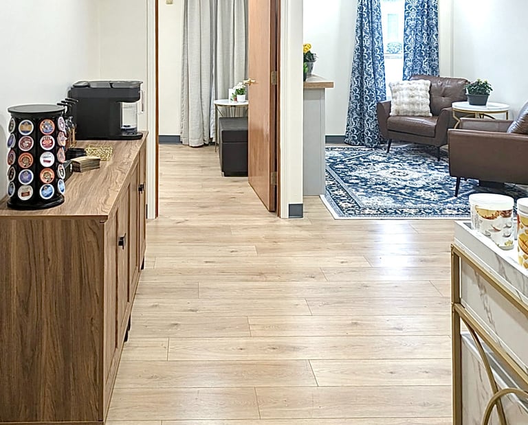 Modern office waiting room with wood floors, blue patterned rug, and brown leather armchairs.