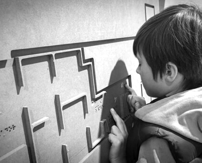 Niewidomy chłopiec odczytuje makietę, na której umieszczono napisy w brajlu