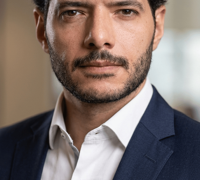 Professional portrait of a businessman with dark hair and a beard wearing a navy blue suit jacket.