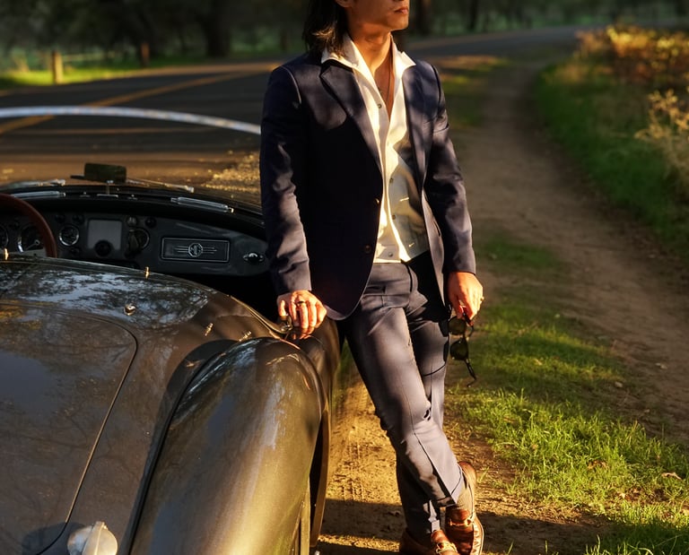 A man leaning against the passenger side of a 1958 MG MGA Roadster in a park during golden hour.