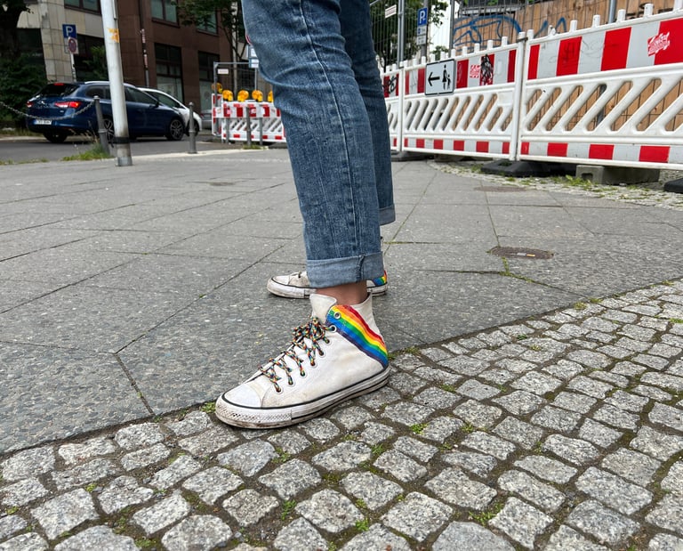 Foto von weißen Turnschuhen mit Regenbogenaufdruck und Regenbogenschnürsenkeln.