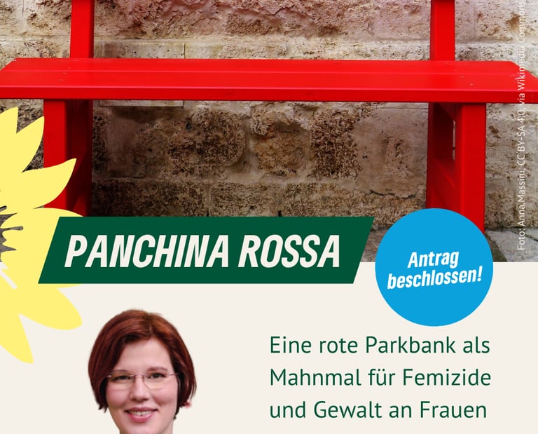 Foto einer roten Parkbank vor einer Mauer.