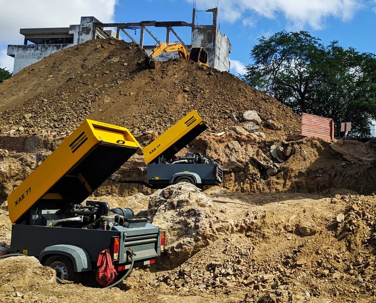 Dois compressores amarelos em uma obra de terraplanagem, realizando serviço de desmonte de rochas