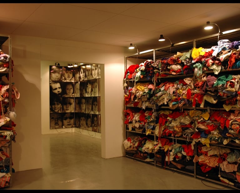 Christian Boltanski art installation featuring stacks of used clothing and a grid of children's portraits.