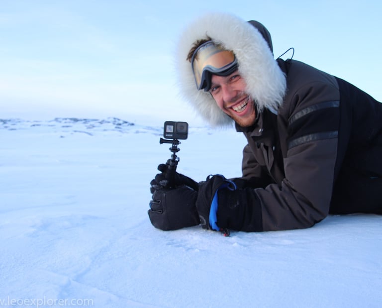 Un explorateur souriant, vêtu d'une parka en fourrure, filme un paysage arctique sur la neige
