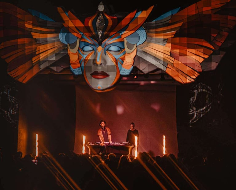 DJs performing atBUMI festival under a large, illuminated tribal mask stage installation.