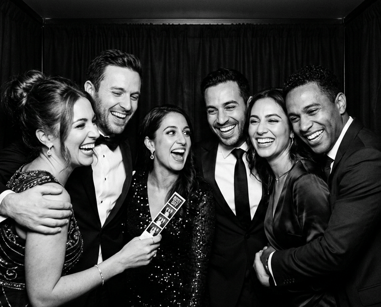Black and white photo of smiling friends celebrating in a wedding photo booth with event props.