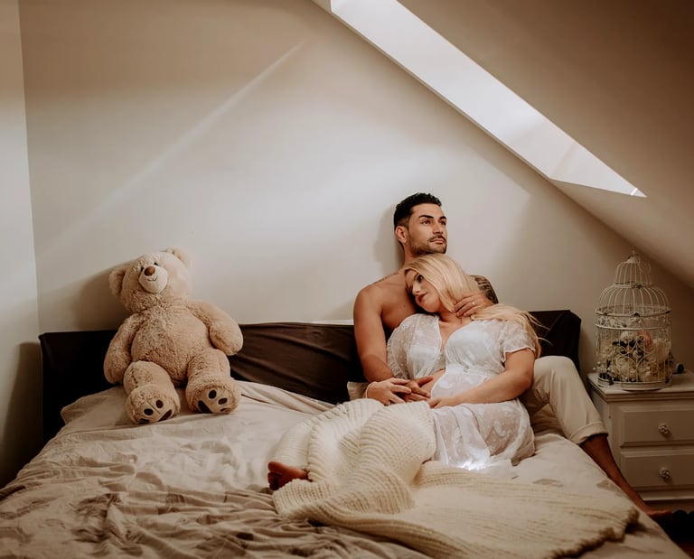 une femme enceinte pose dans son lit avec son conjoint pour une séance photo grossesse