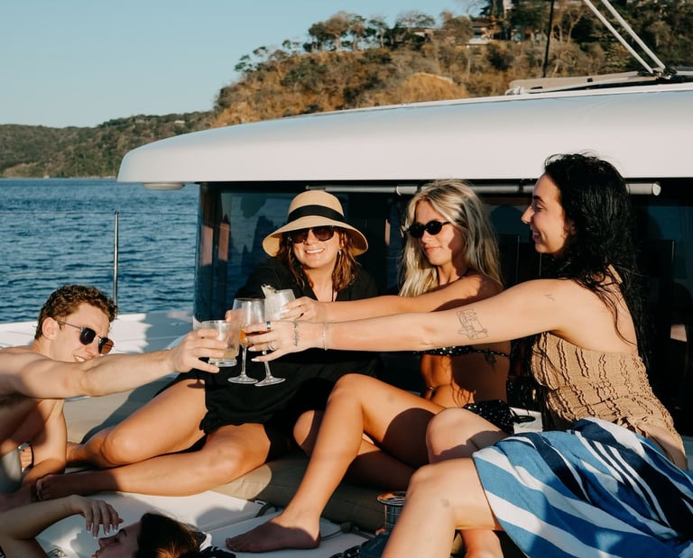 Group of friends toasting with cocktails during sunset cruise on luxury catamaran in Papagayo
