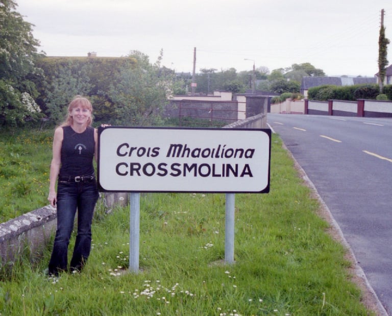 Annie of Crossmolina Band standing next to the welcome sign, County Mayo, Republic of Ireland.
