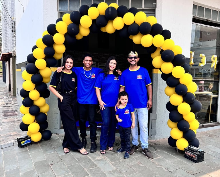 4 adultos e 1 criança com uniformes azuis, em frente a loja de baterias automotivas