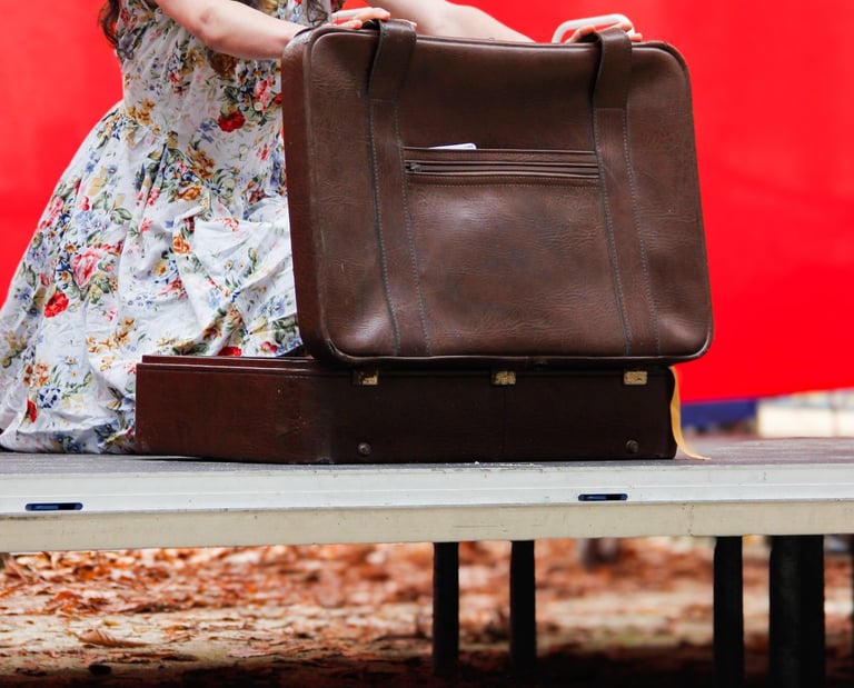comédienne chanteuse sur scène équipée d'un micro serre tête, en train d'ouvrir une valise
