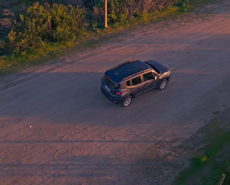 Vue aérienne par drone d’une Jeep Renegade sur un chemin en gravier à la golden hour