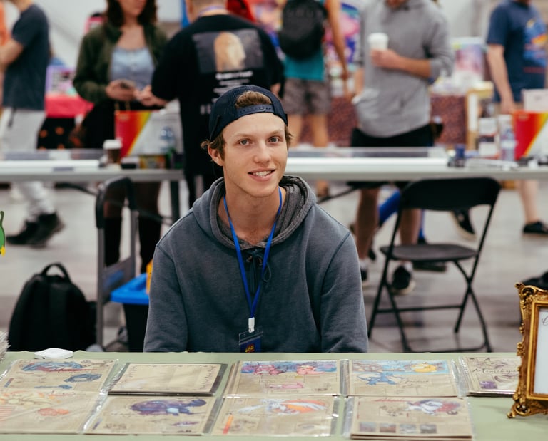 A smiling vendor sits at a table in front of his trading cards for sale.
