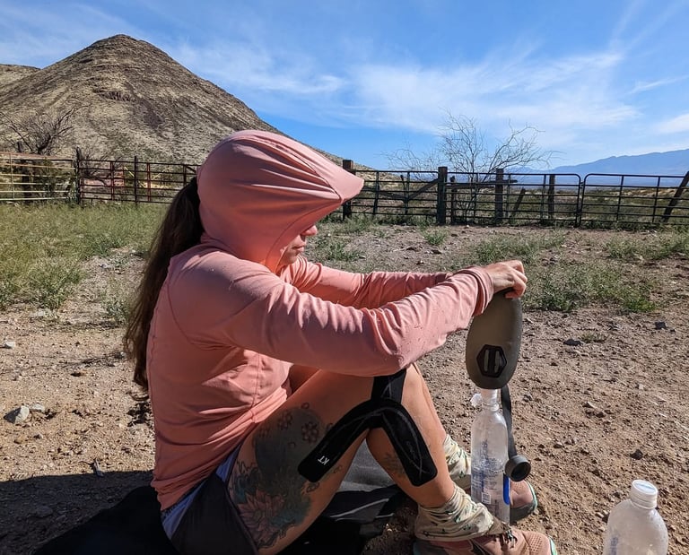 Samantha in a pink sun hoodie filters water in a Hydrapak seeker bladder in the New Mexican desert.