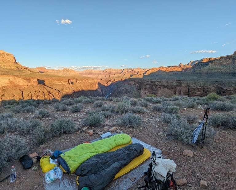 A cowboy camp setup with a Feathered Friends sleeping bag near a cliff in the Grand Canyon.