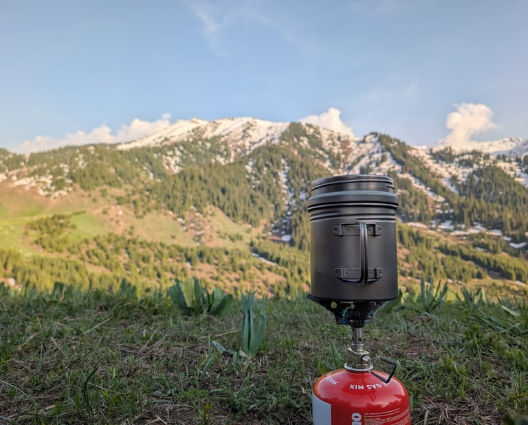 Portable camping stove and Vargo BOT on a grassy mountain ridge with snowy peaks in the background.