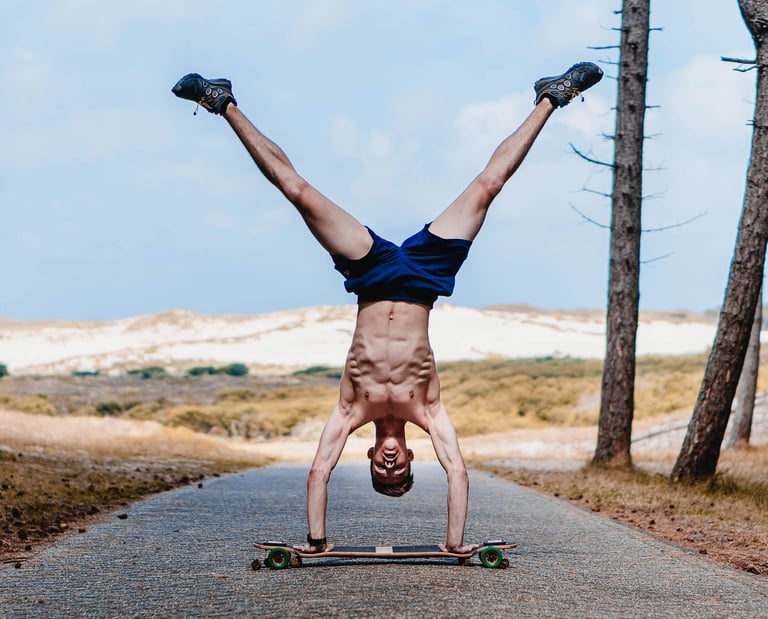 Mann macht Handstand auf einem Longboard auf einem Waldweg. Kreatives Sportfoto von Joel Pingel.