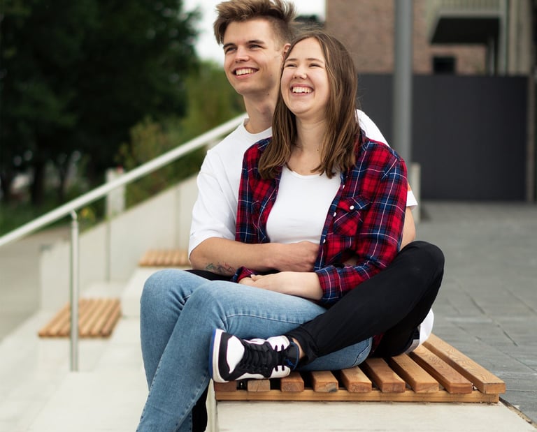 Lachendes Paar sitzt entspannt auf einer Bank bei einem urbanen Paarshooting. Foto von Joel Pingel.