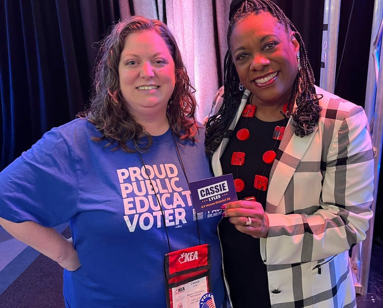 Woman in blue shirt standing with a black woman holding a campaign sticker