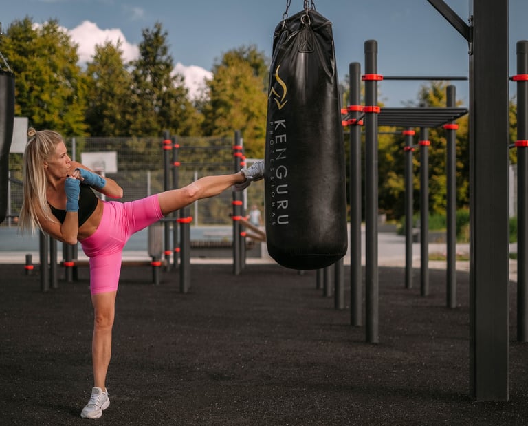 Femme donnant un coup de pied sur un sac de frappe Kenguru Pro dans un espace d’entraînement extérieur.