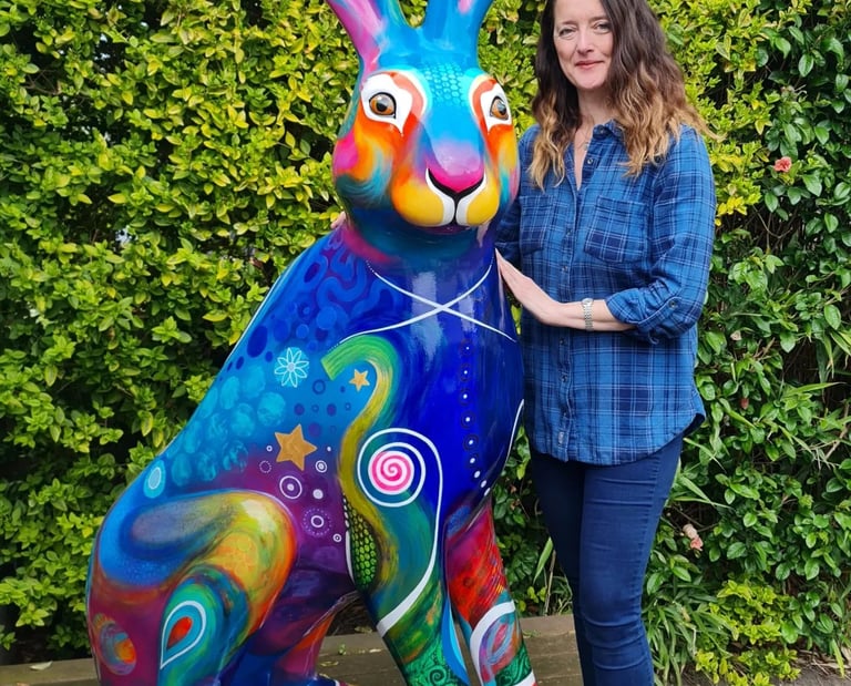 Alanda Calmus artist stands beside a large, brightly painted Big Hop Trail Hare sculpture