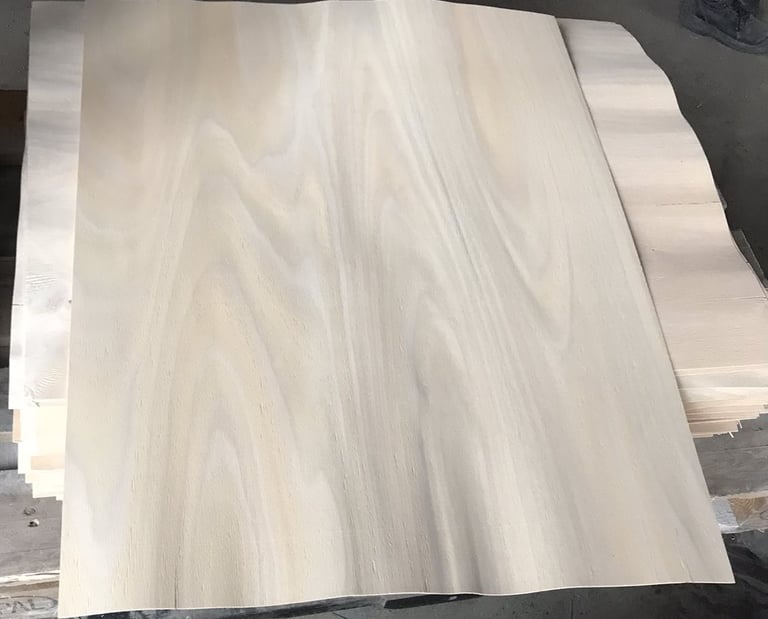 Stacked thin natural wood veneer sheets with light grain patterns for furniture making and woodworking.