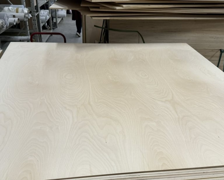 Close-up of a smooth birch plywood sheet with visible wood grain in a lumber warehouse.