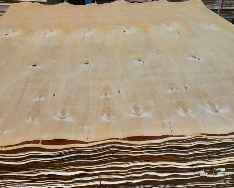 Stack of thin natural wood veneer sheets in a lumber processing factory warehouse.
