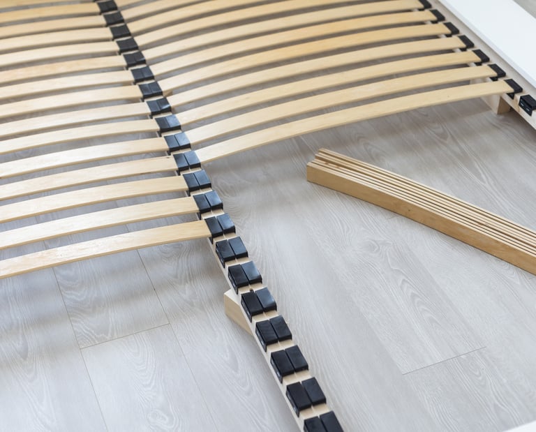 Close-up of a wooden slatted bed base frame being assembled on a light laminate floor.