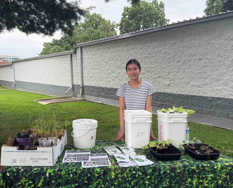 A high school student standing behind a table with hydroponic grow buckets and plant seedlings