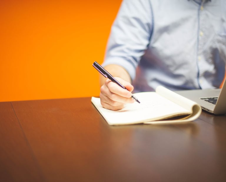 A person at a desk with laptop, pen and paper