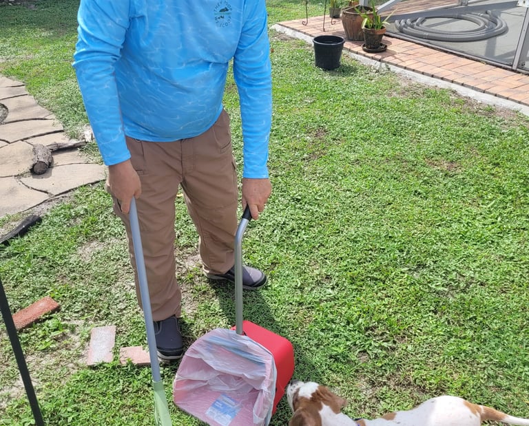 Robert using a sanitized scooper to remove waste from a customers back yard, small dog watching him