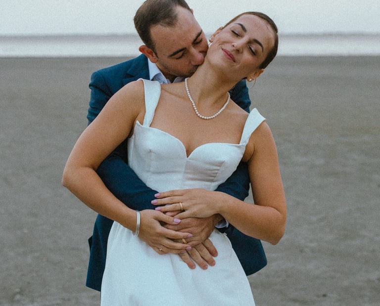un marié qui embrasse sa femme dans le cou sur la plage